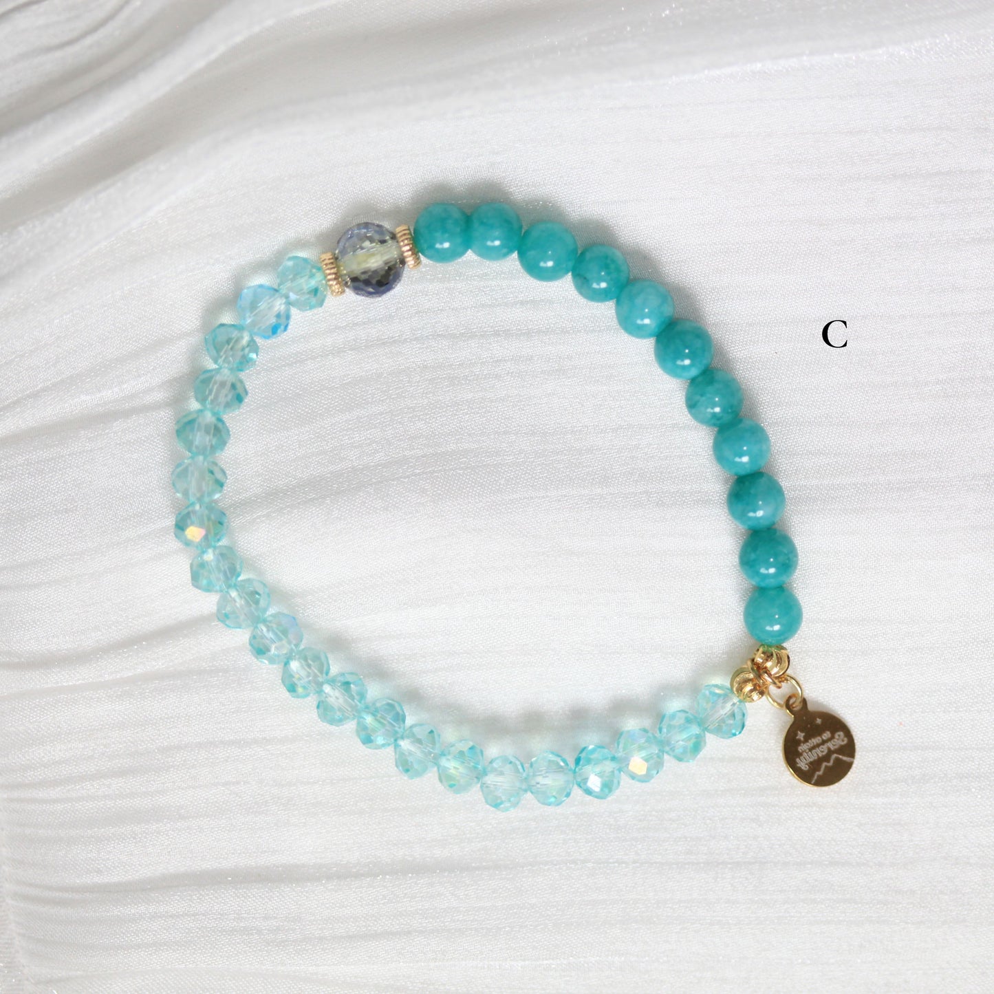 Turquoise beaded bracelet with a gold tag on a white fabric background