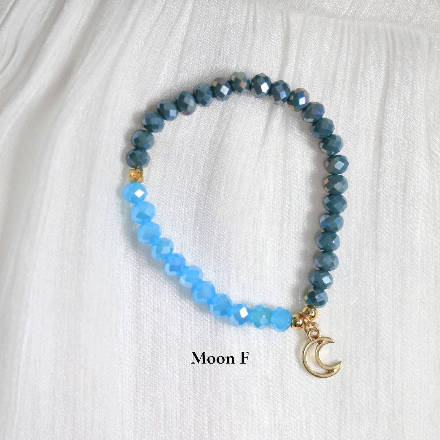 Dreamersside Blue beaded tsabih bracelet with a gold moon charm on a white fabric background