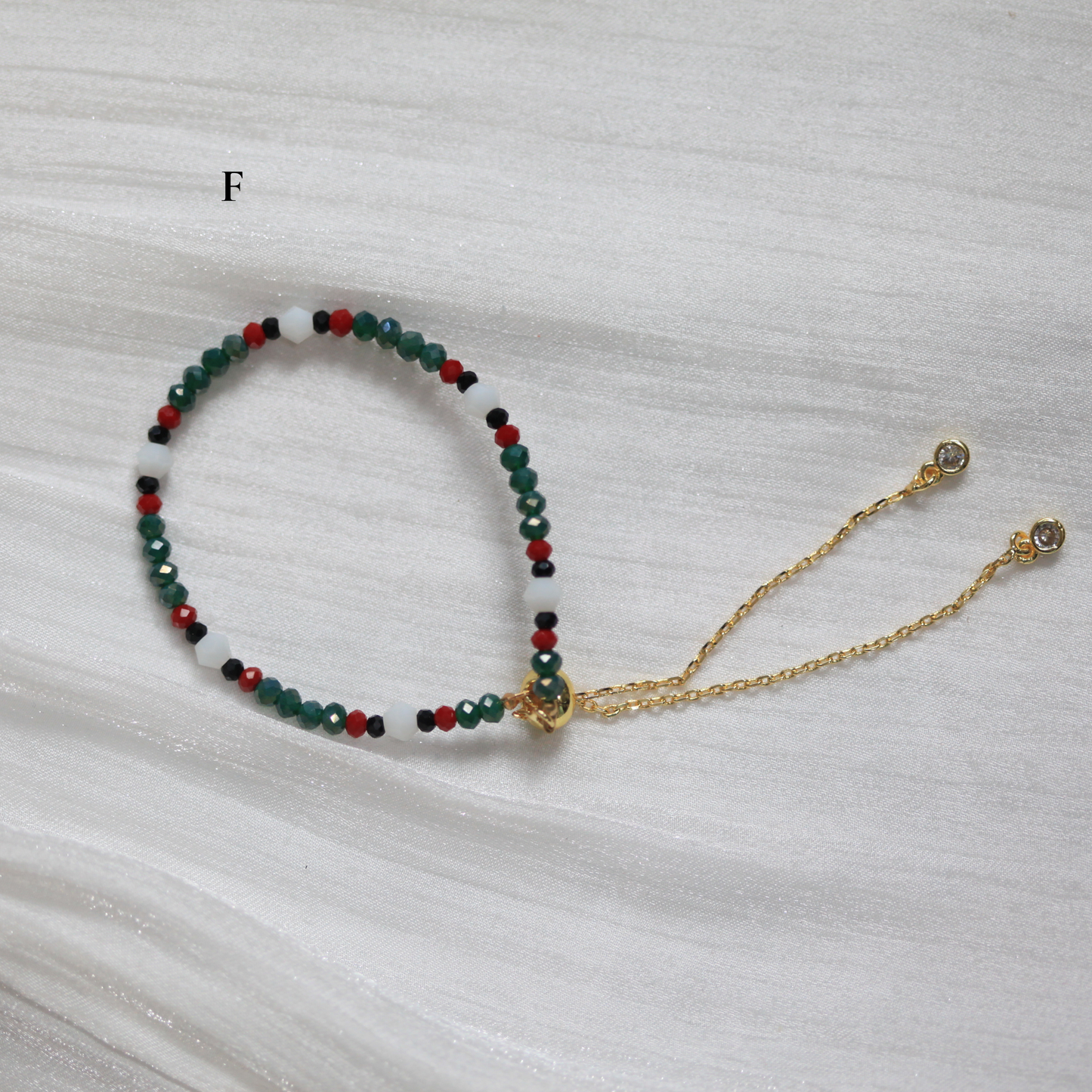 Multicolored beaded bracelet with a gold chain on a white fabric background
