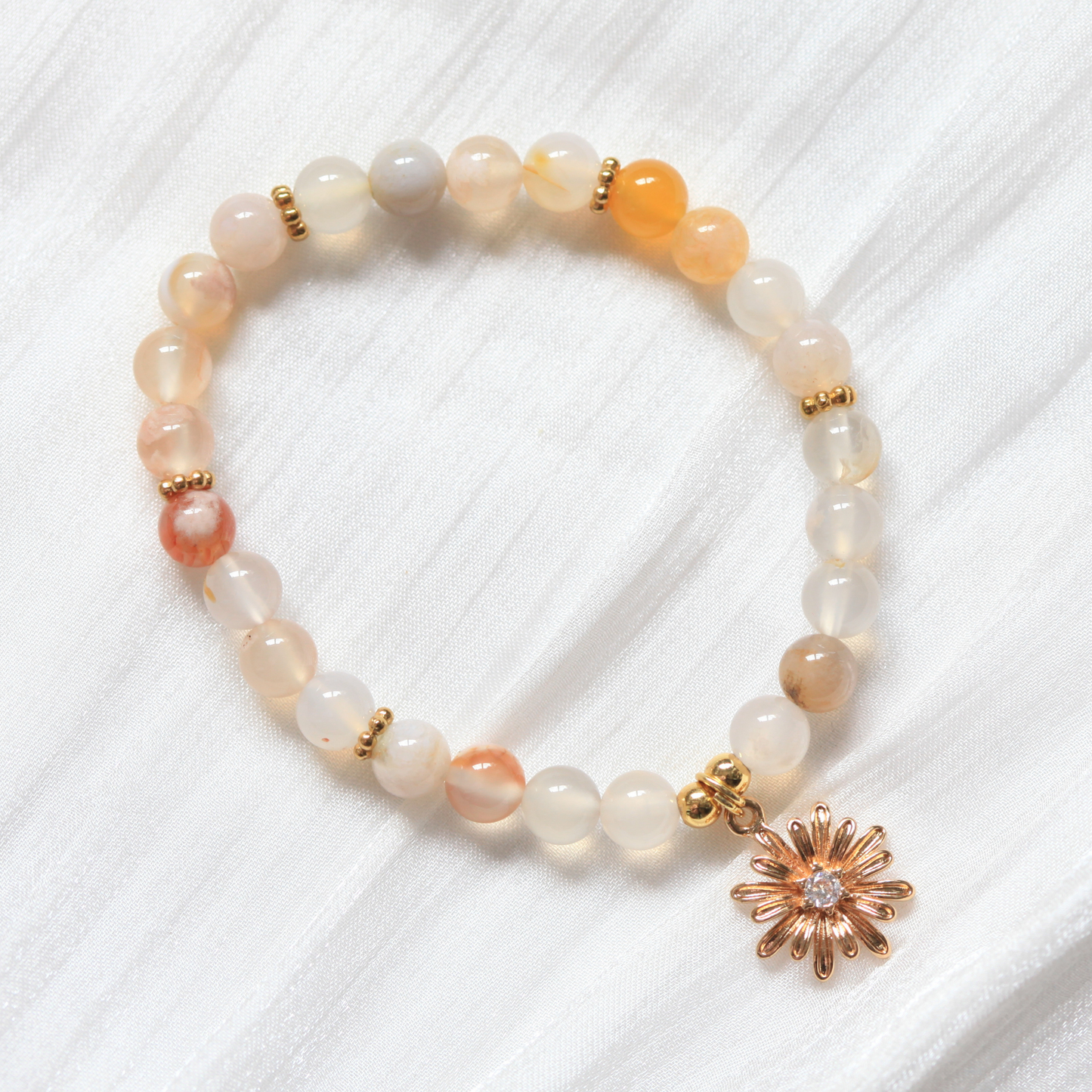 Beaded bracelet with a gold flower charm on a white textured background