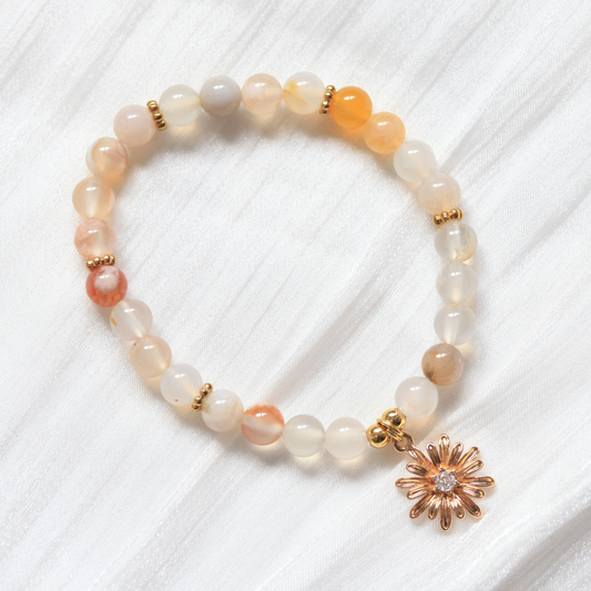 Beaded bracelet with a gold flower charm on a white textured background
