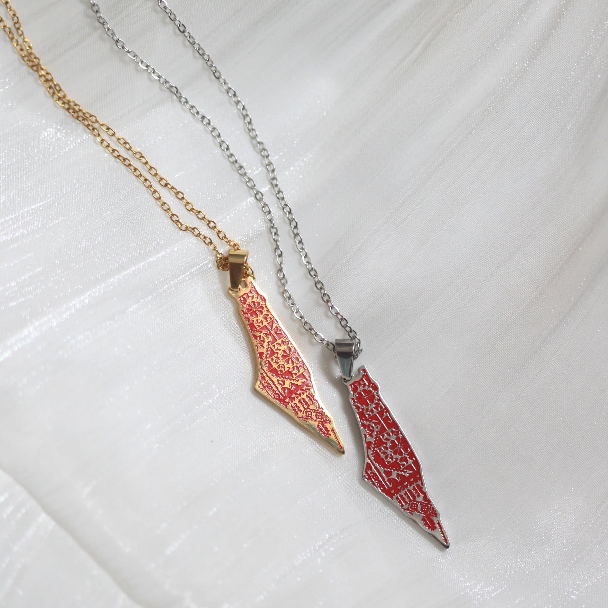 Two necklaces with red and gold pendants on a white textured background