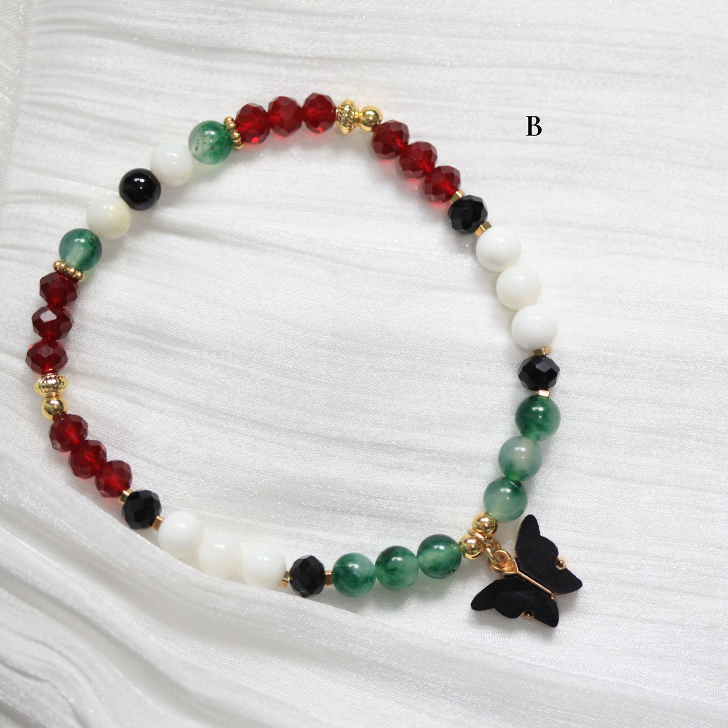 Tasbih Beaded bracelet with colorful beads and a black butterfly charm on a white fabric background