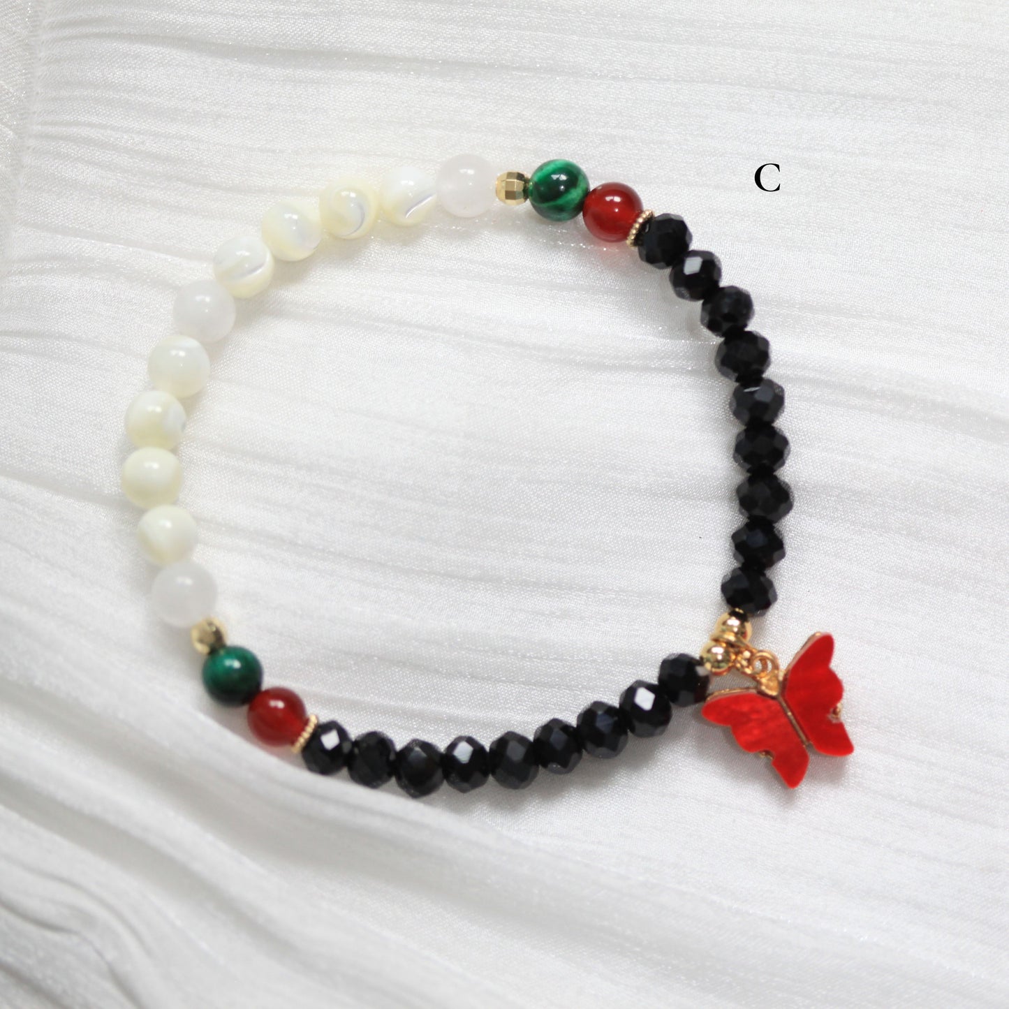Tasbih Bracelet with beads and a red butterfly charm on a white fabric background