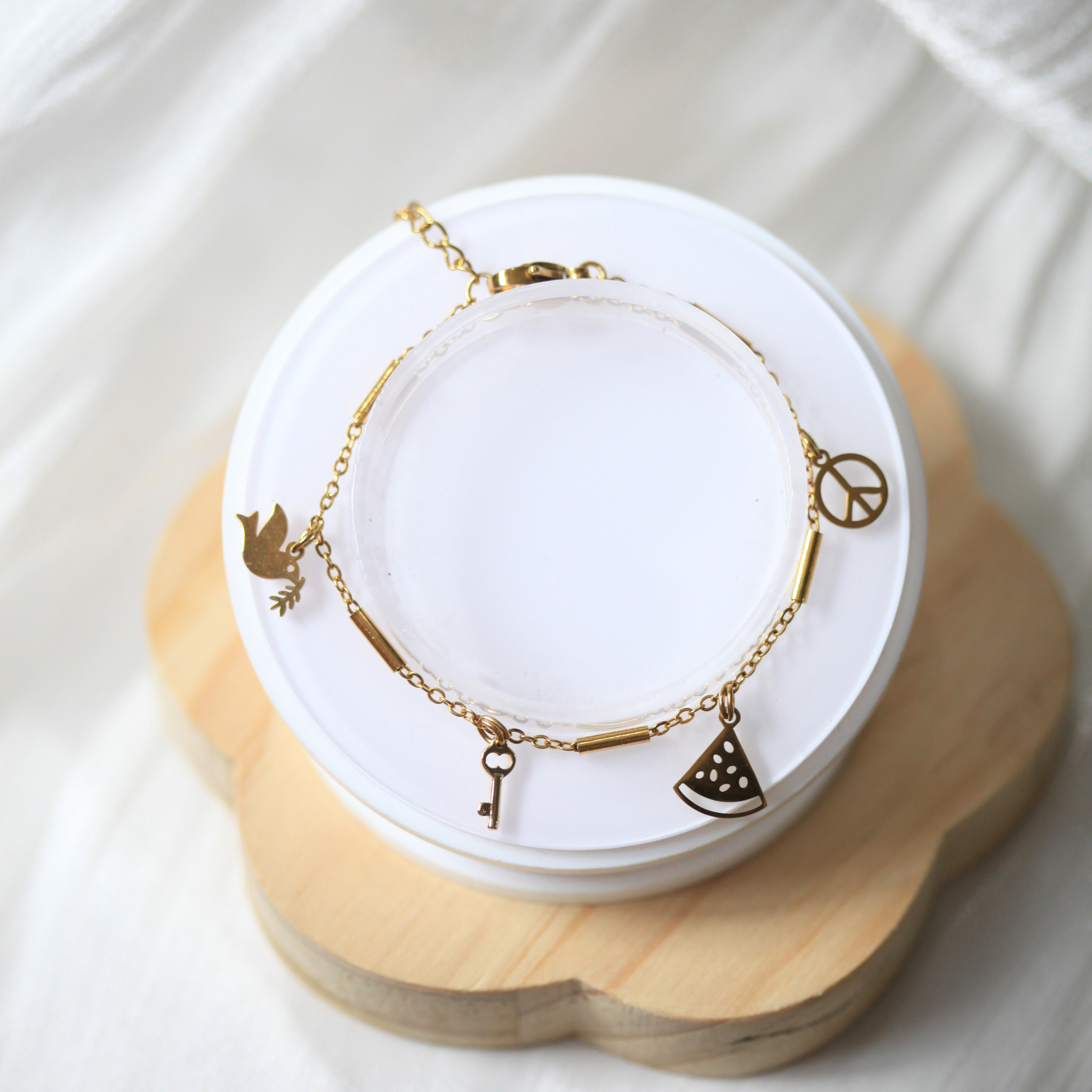 Gold bracelet with charms on a white jewelry display stand. 