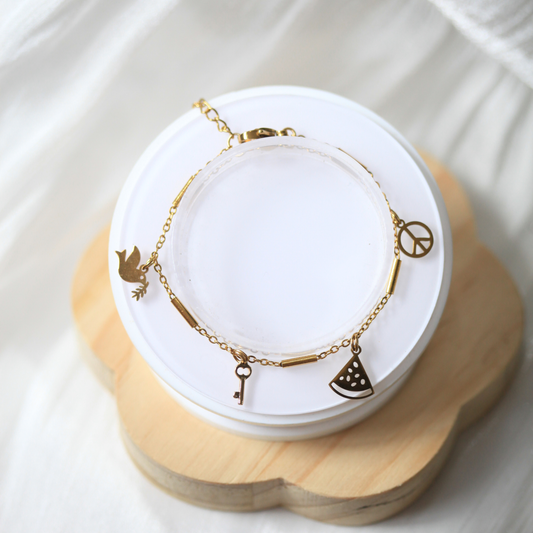 Gold bracelet with charms on a white jewelry display stand. 