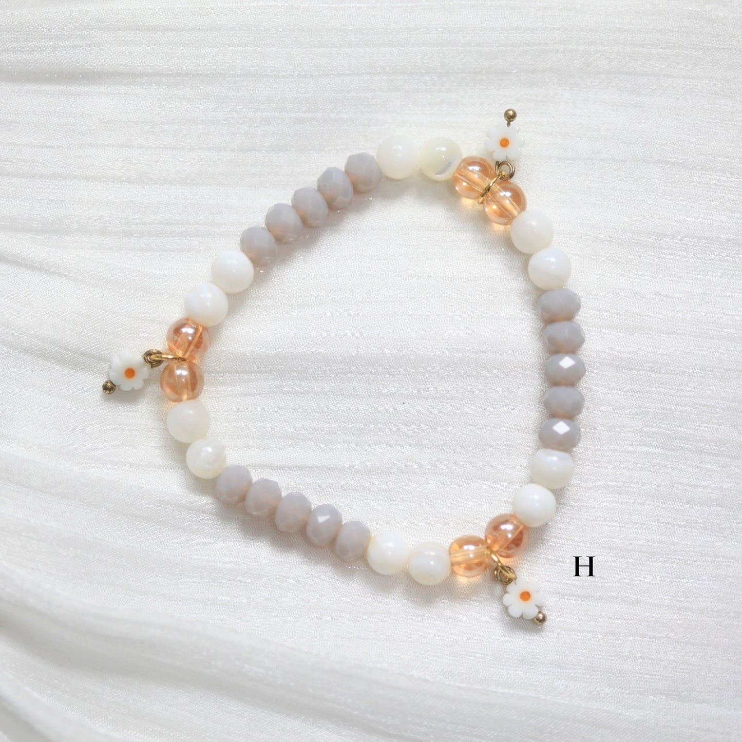 Beaded tasbih bracelet with white, beige, and gold beads on a white textured background