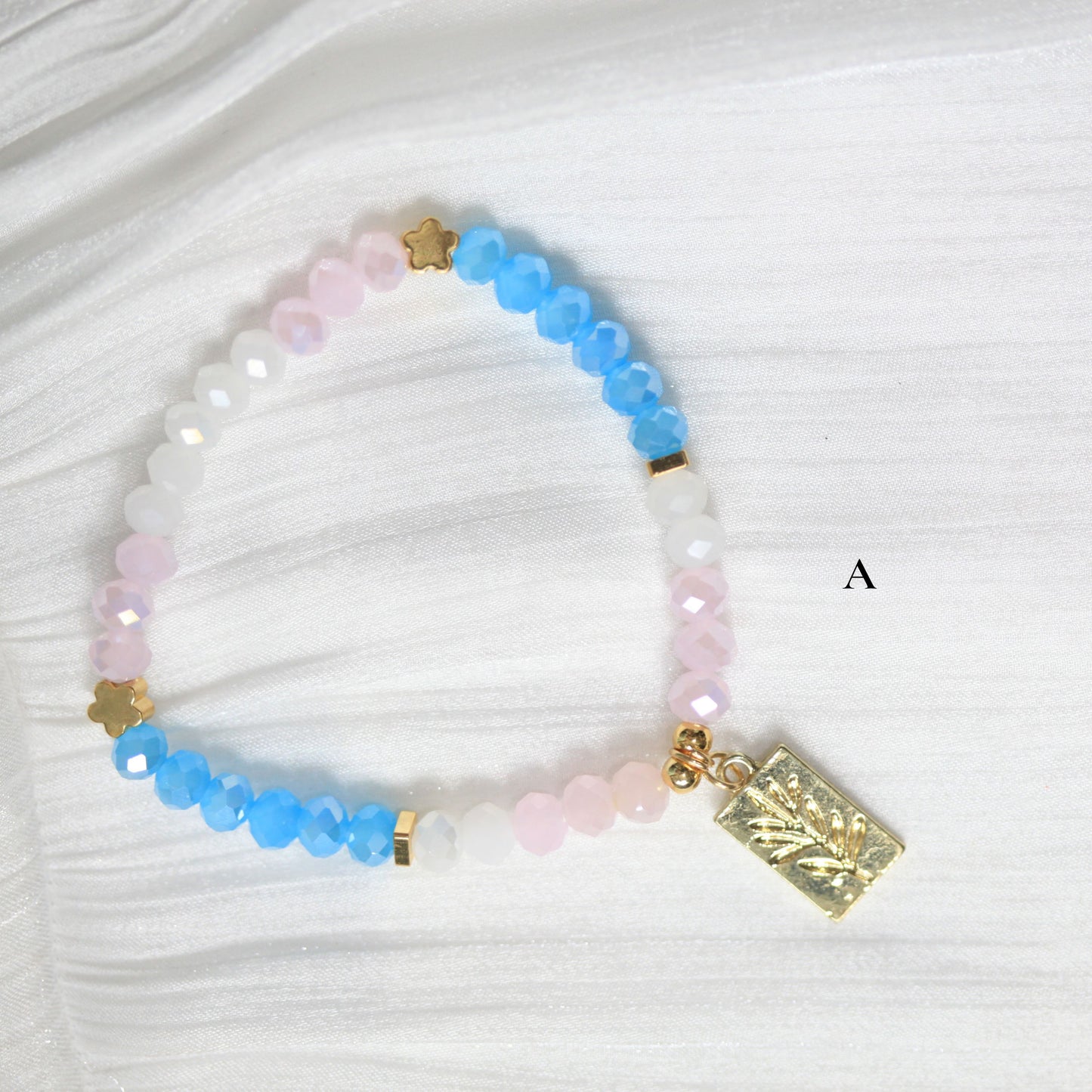 Tasbih Beaded bracelet with blue, pink, and gold elements on a white fabric background