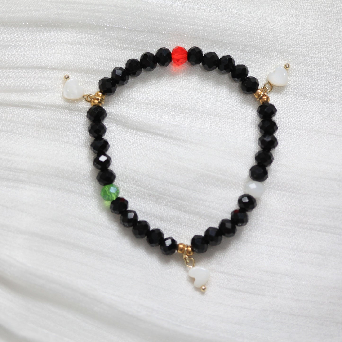 Black beaded bracelet with gold and white accents on a white fabric background