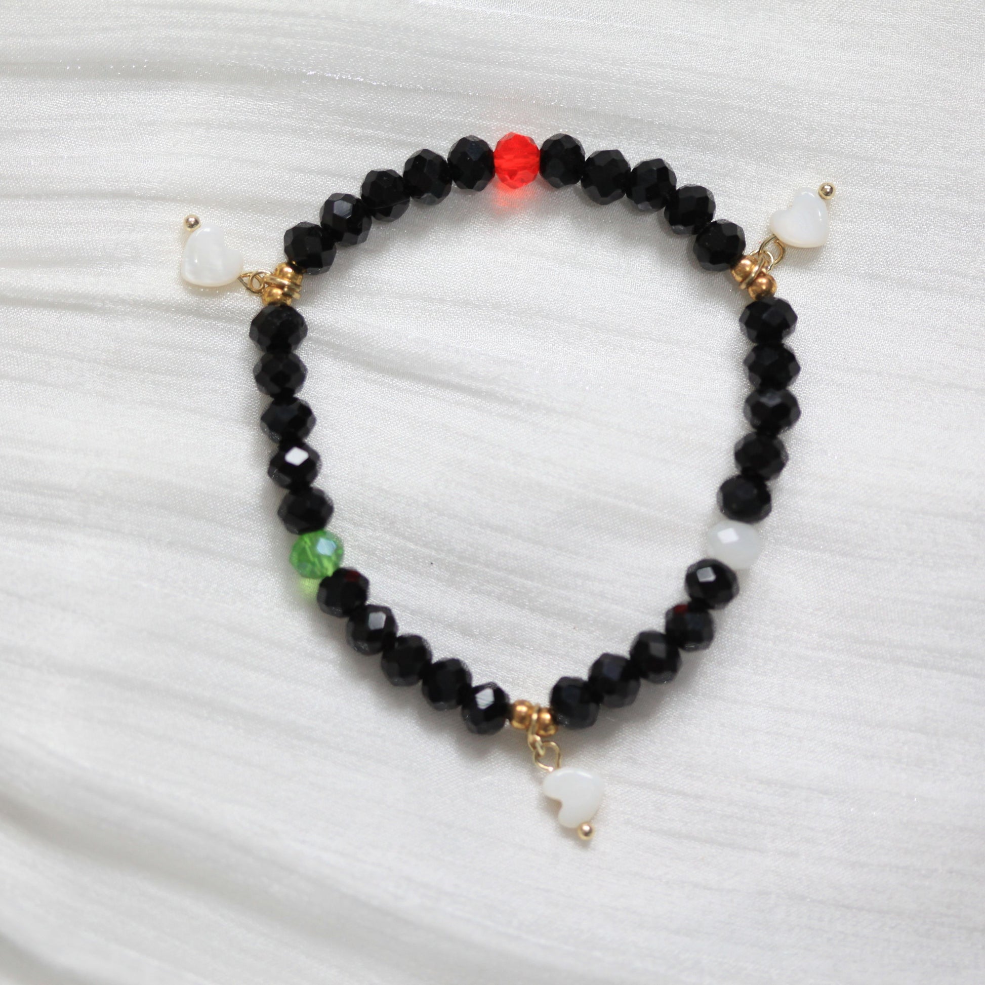 Black beaded bracelet with gold and white accents on a white fabric background