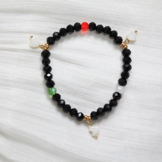 Black beaded bracelet with gold and white accents on a white fabric background