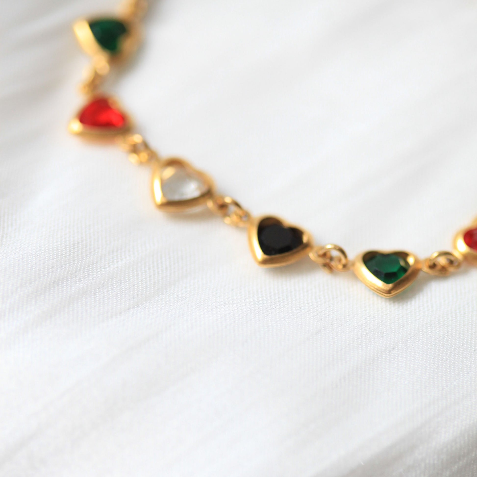 Gold necklace with heart-shaped gemstones on a white background