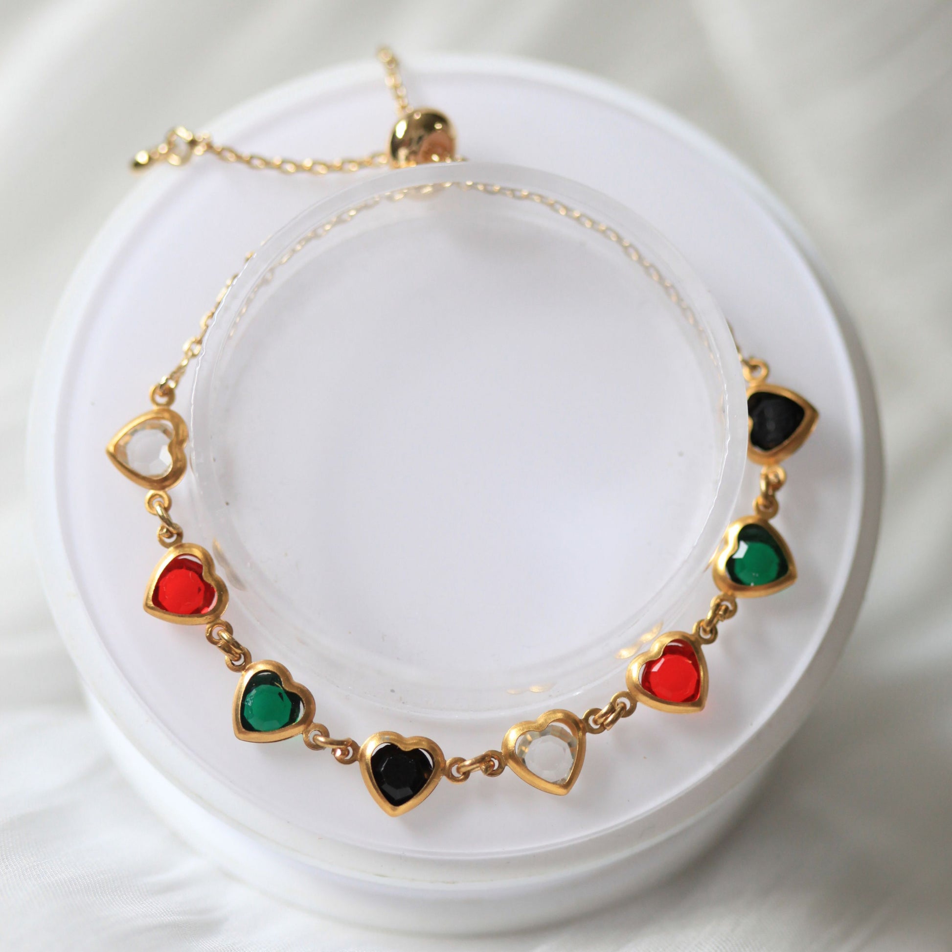 Bracelet with heart-shaped pendants in red, green, and black on a white background
