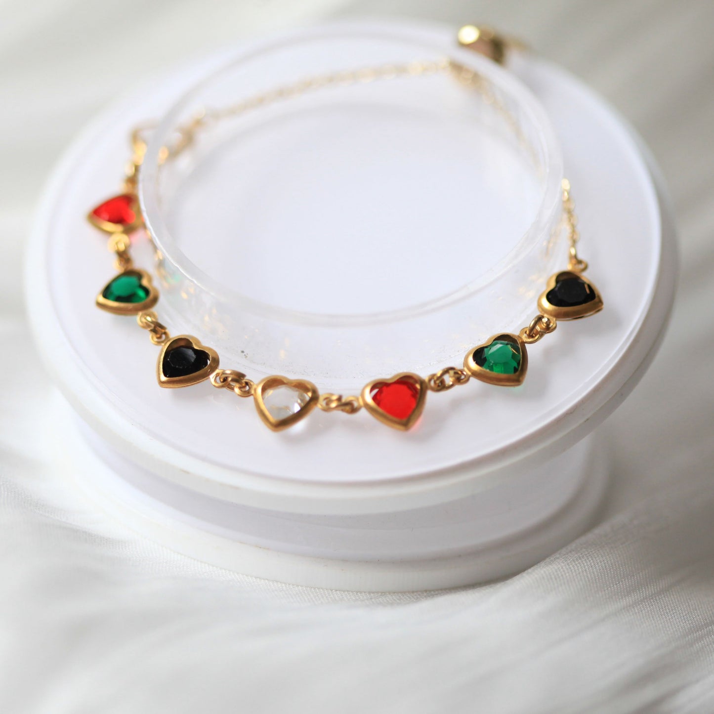 Gold bracelet with heart-shaped gemstones on a white stand