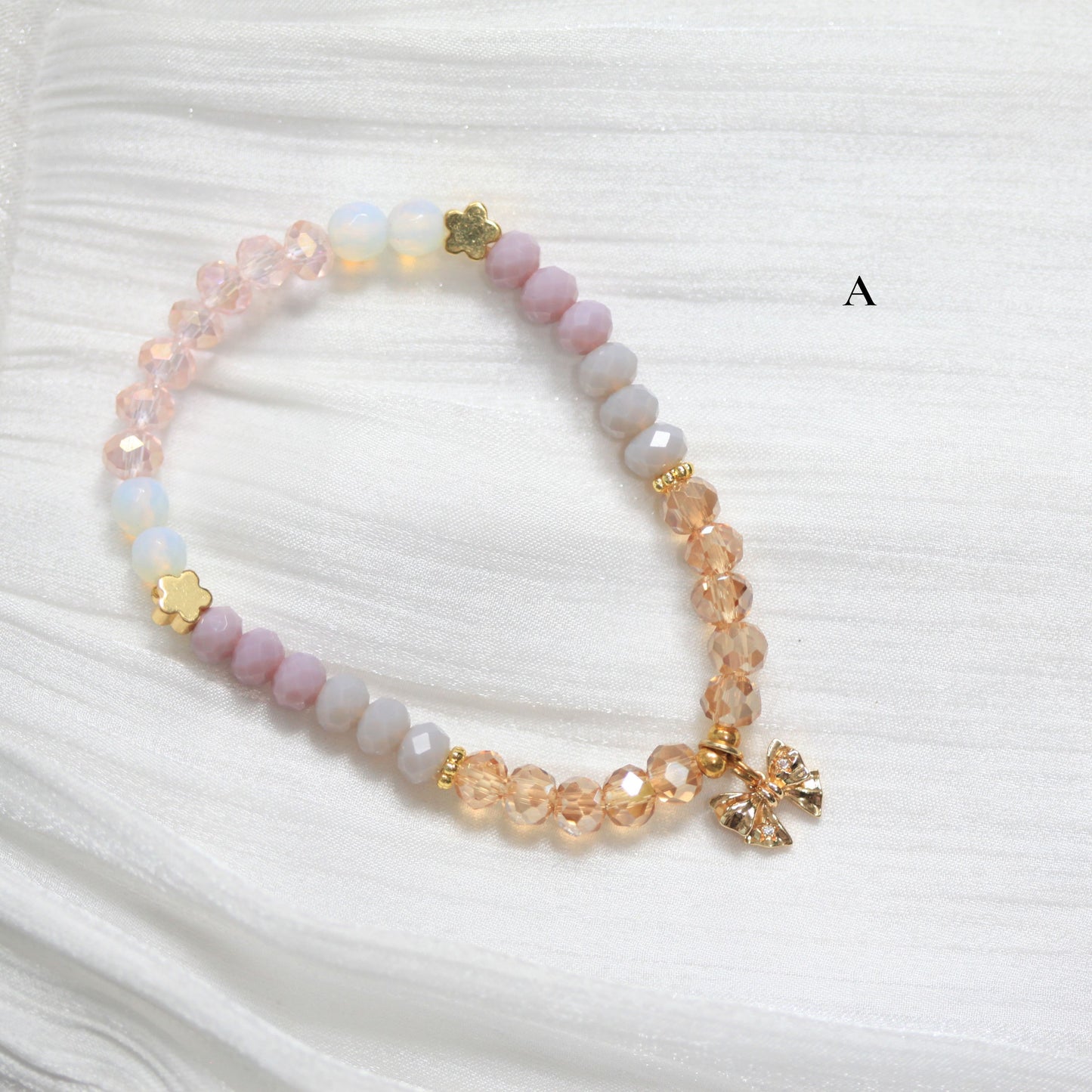 Beaded bracelet with ribbon-shaped charms on a white fabric background
