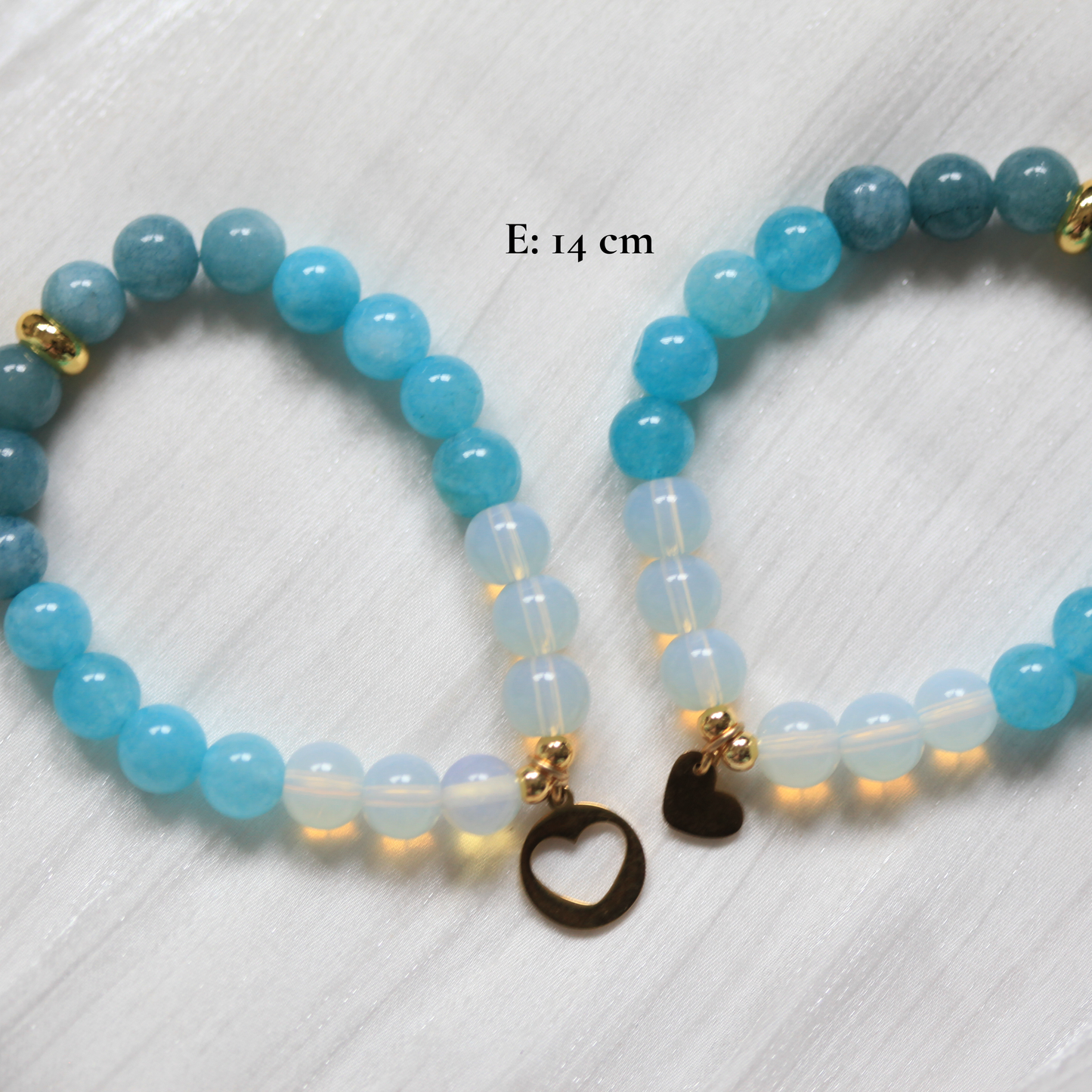 Two blue beaded bracelets with heart-shaped charms on a white textured background