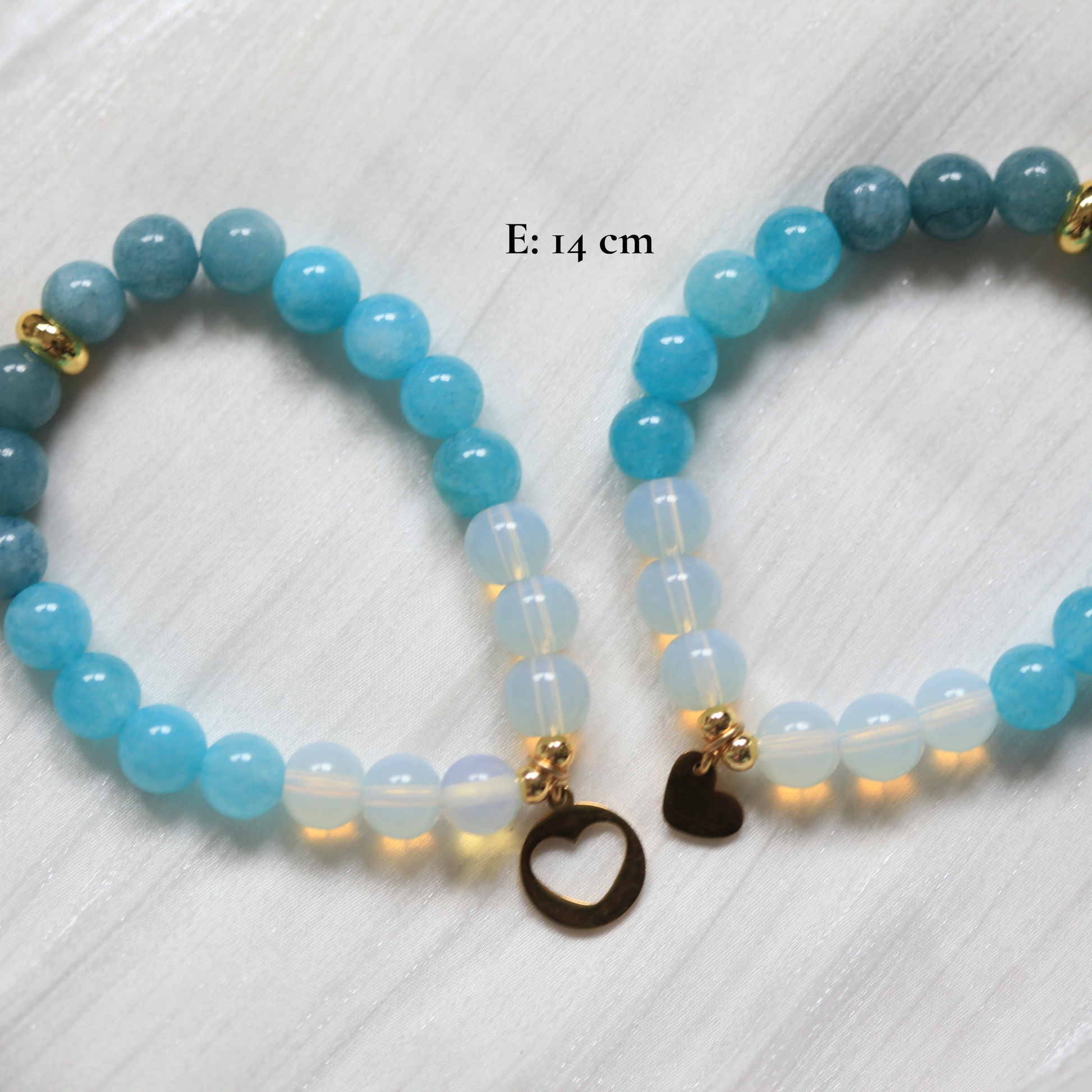 Two blue beaded bracelets with heart-shaped charms on a white textured background