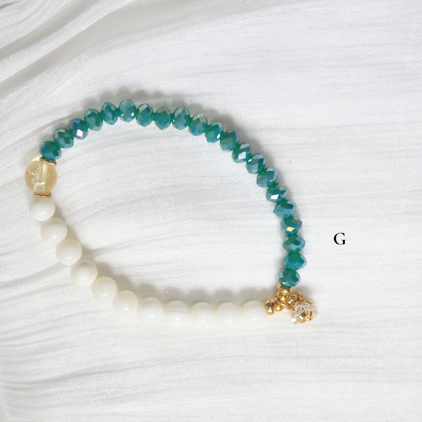 Bracelet with white beads and blue-green beaded extensions on a white background