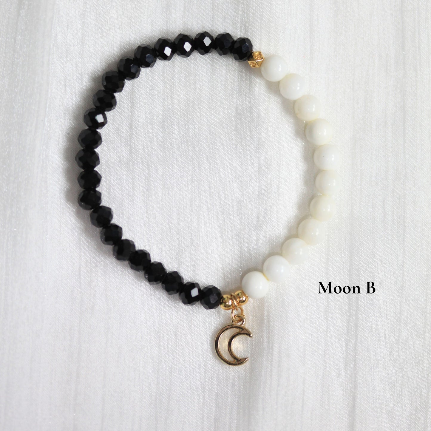 Black tasbih beaded bracelet with a gold moon charm on a white textured background
