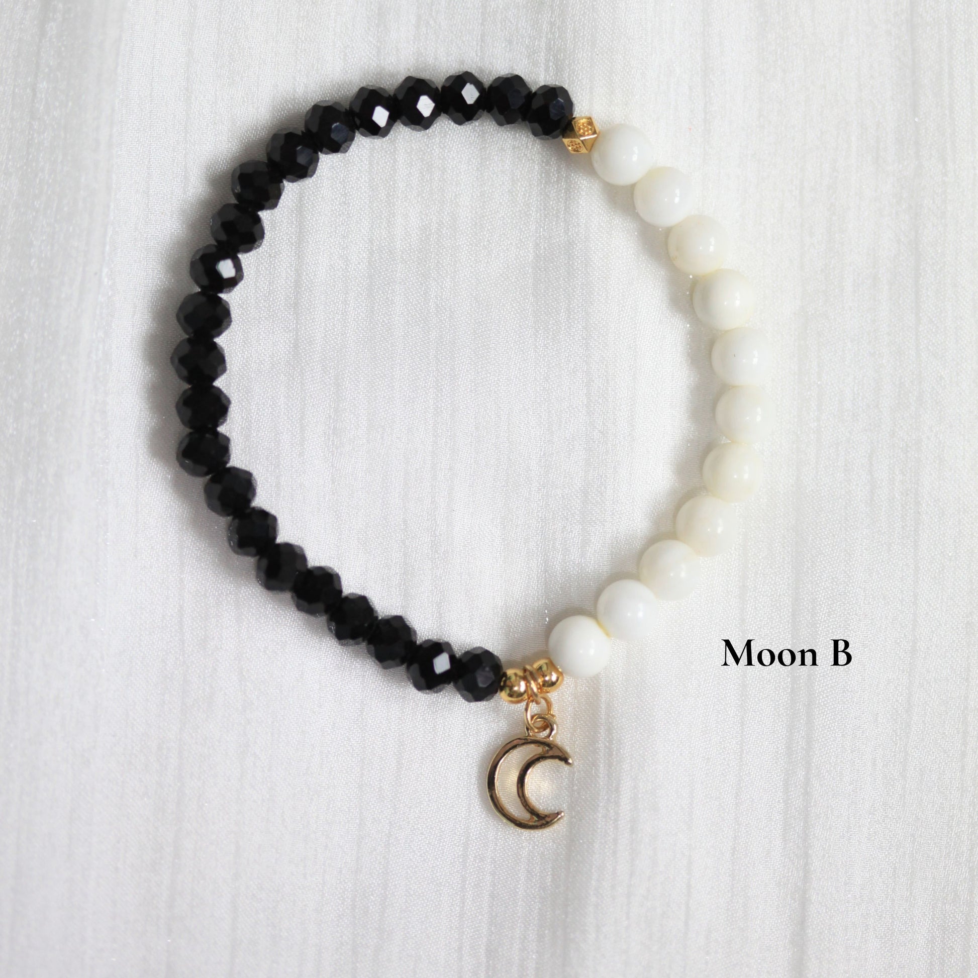 Black tasbih beaded bracelet with a gold moon charm on a white textured background