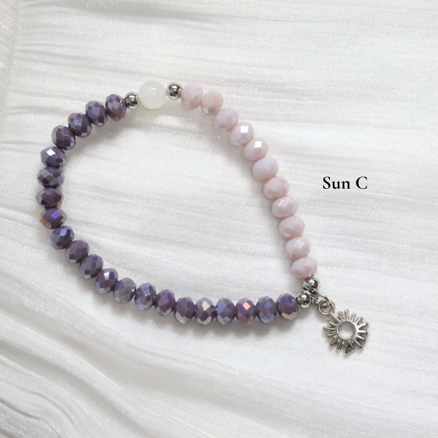 Beaded tasbih bracelet with a sun charm on a white fabric background