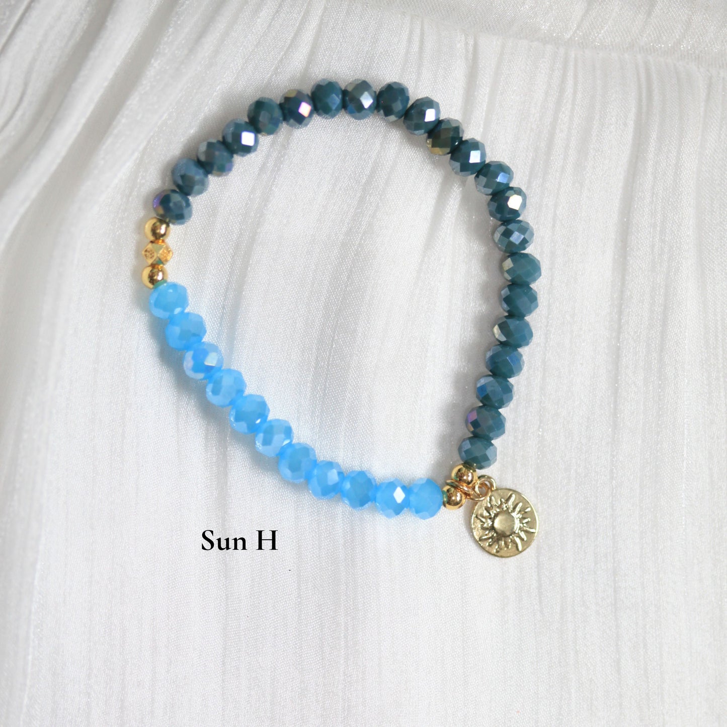 Tasbih Bracelet with blue beads and a gold charm on a white fabric background