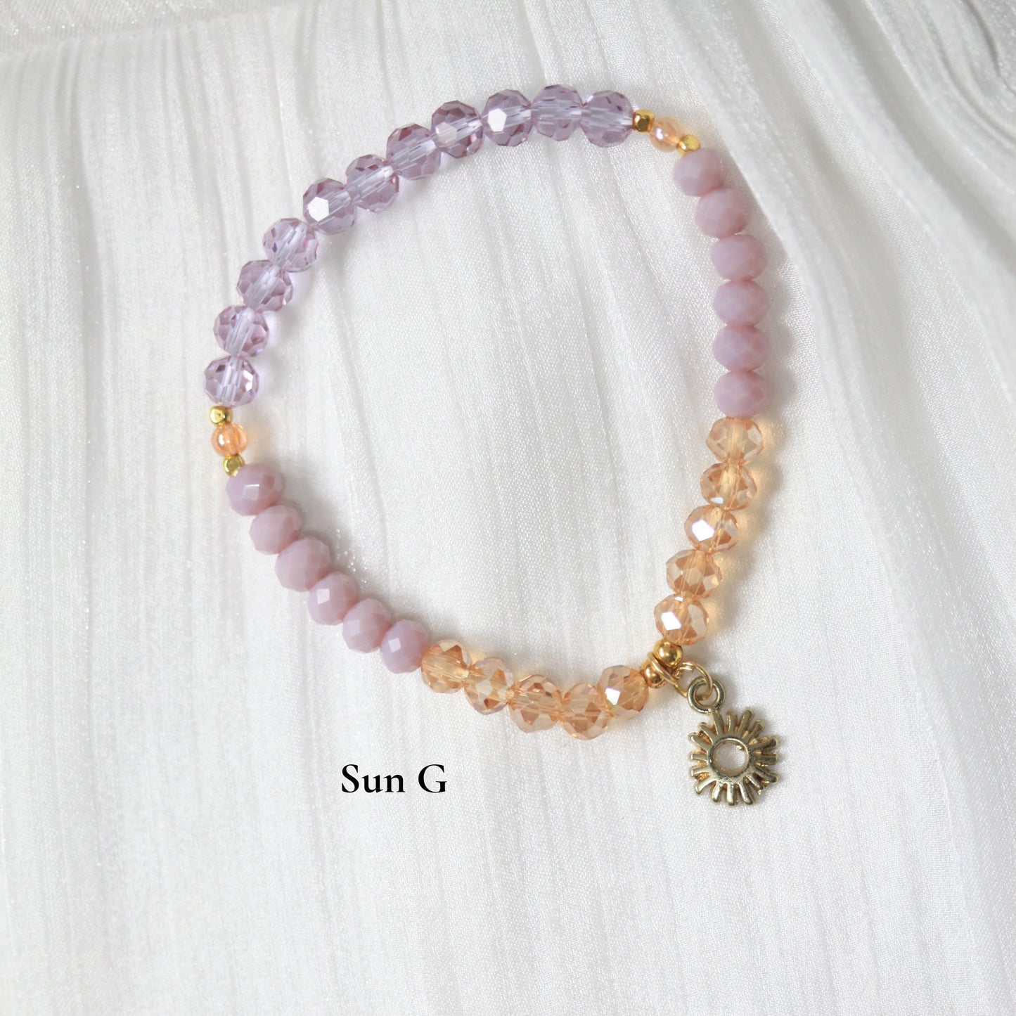 Beaded tasbih bracelet with a sun-shaped charm on a white fabric background