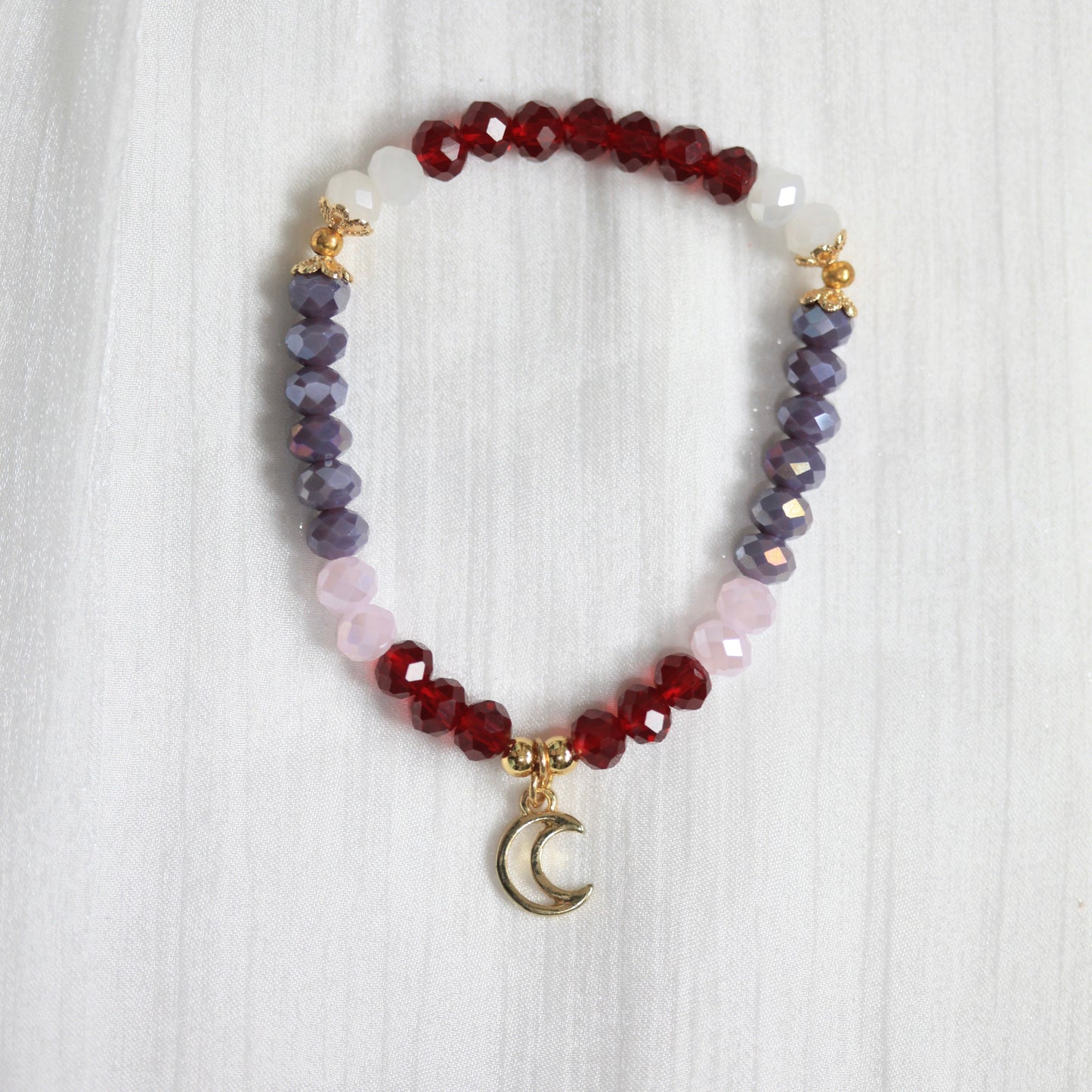 Multicolored beaded tasbih bracelet with a moon charm on a white textured background