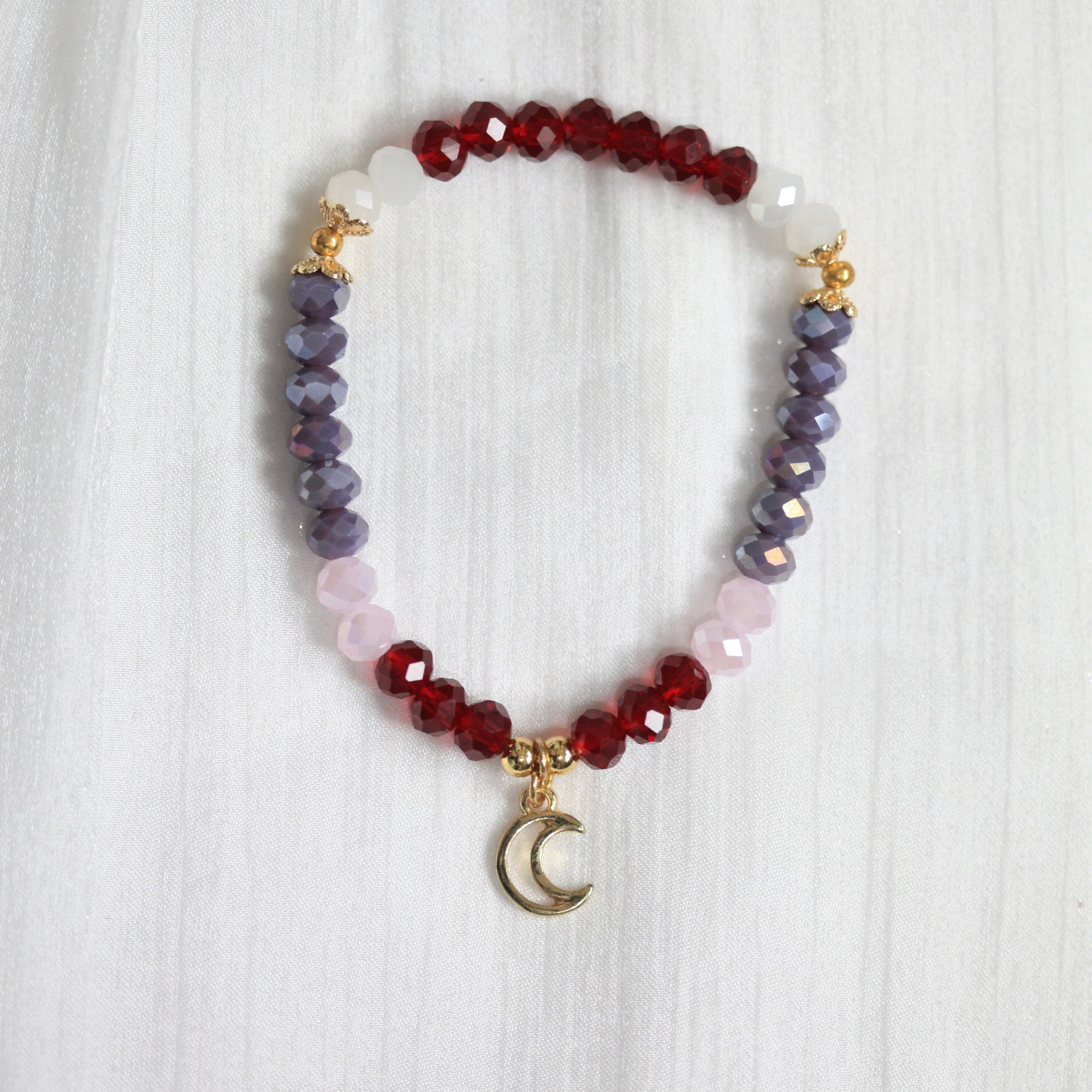 Multicolored beaded tasbih bracelet with a moon charm on a white textured background