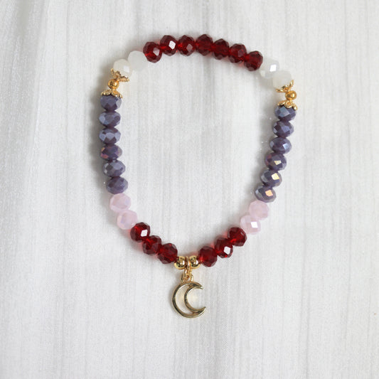 Multicolored beaded tasbih bracelet with a moon charm on a white textured background