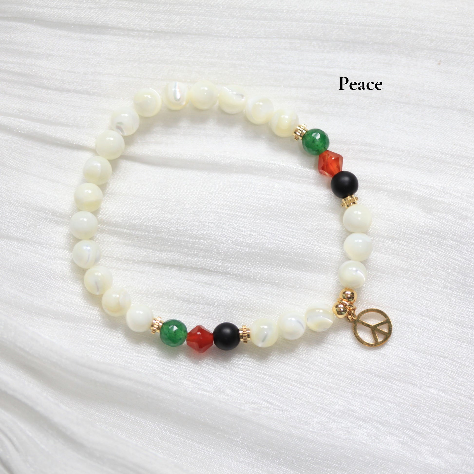 Beaded bracelet with peace charm on a white fabric background