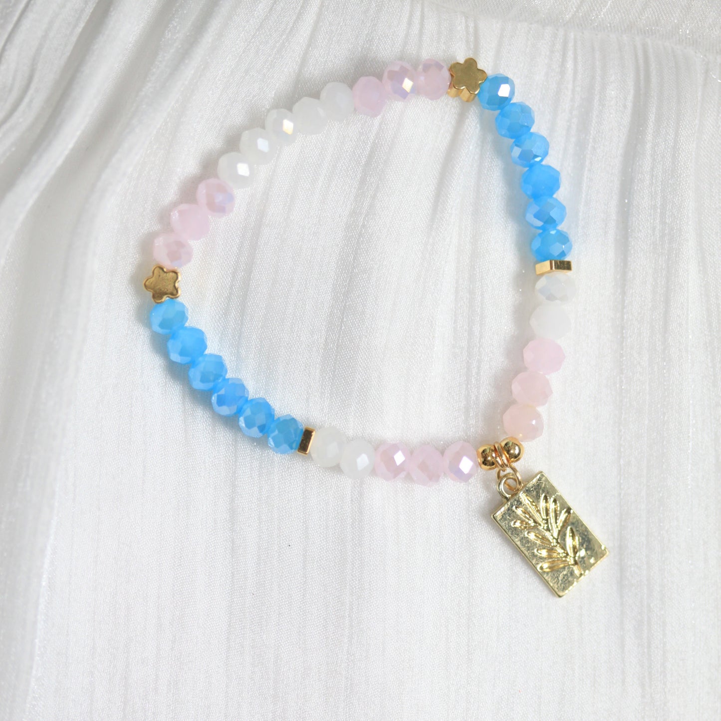 Multicolored beaded bracelet with a gold charm on a white fabric background