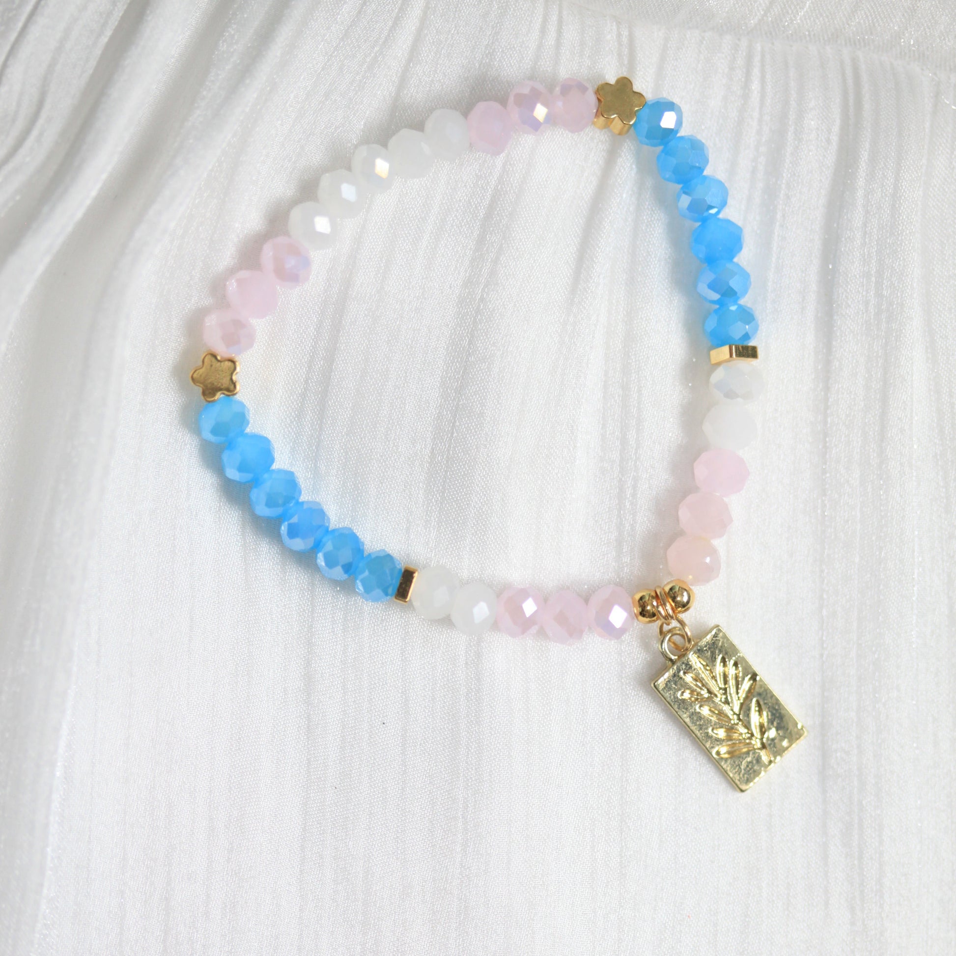 Multicolored beaded bracelet with a gold charm on a white fabric background