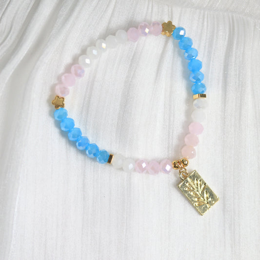 Multicolored beaded bracelet with a gold charm on a white fabric background
