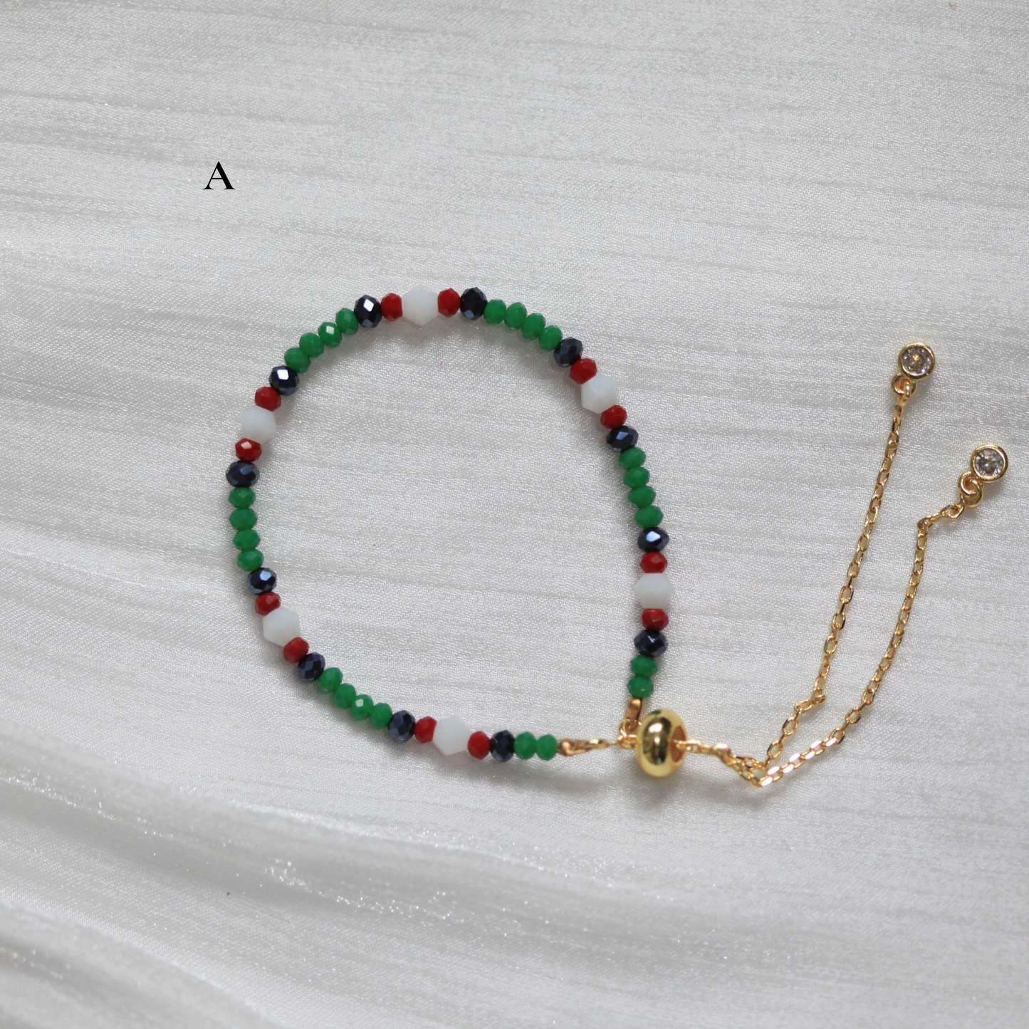 Multicolored beaded bracelet with a gold chain on a light gray background. Tatreez Inspired