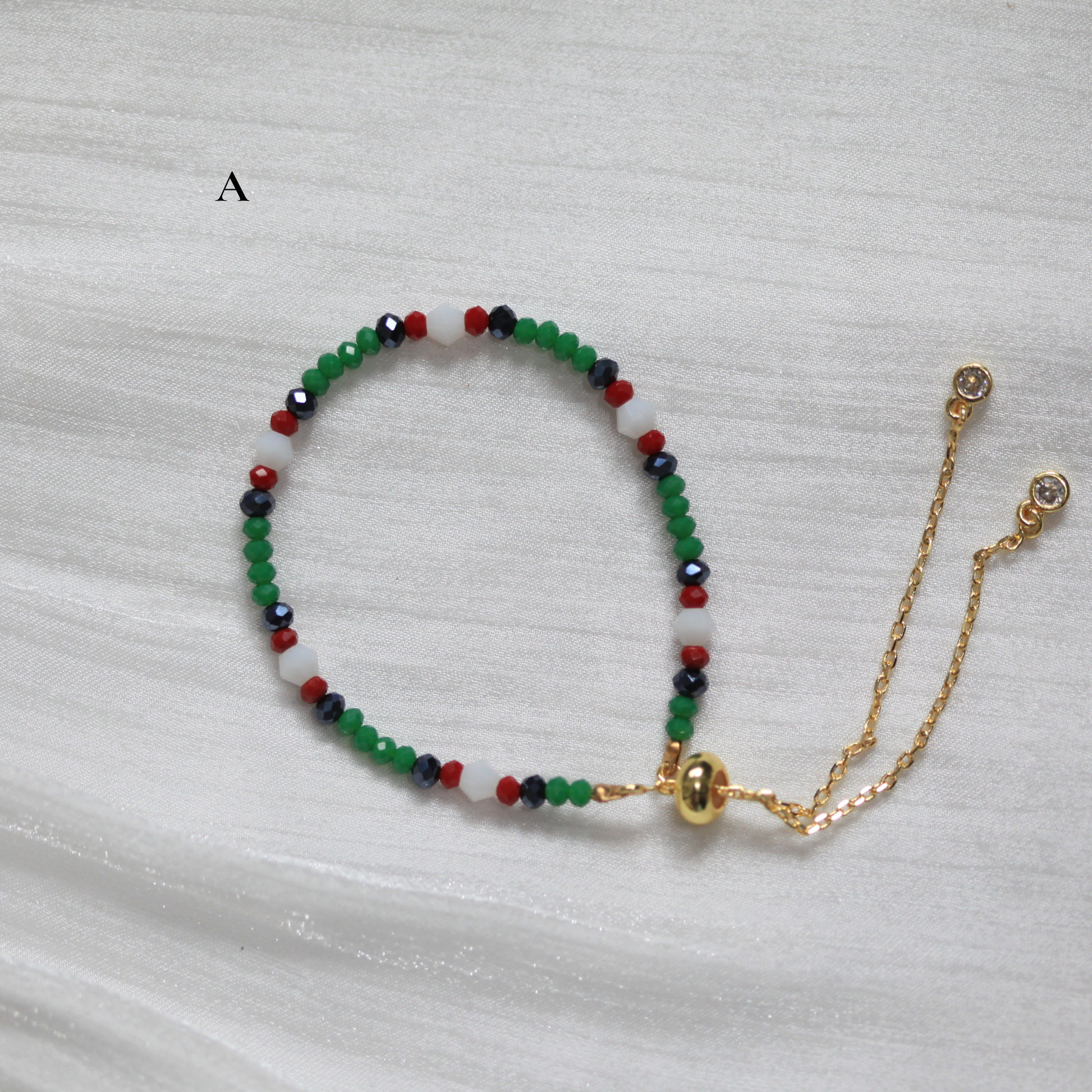 Multicolored beaded bracelet with a gold chain on a light gray background. Tatreez Inspired