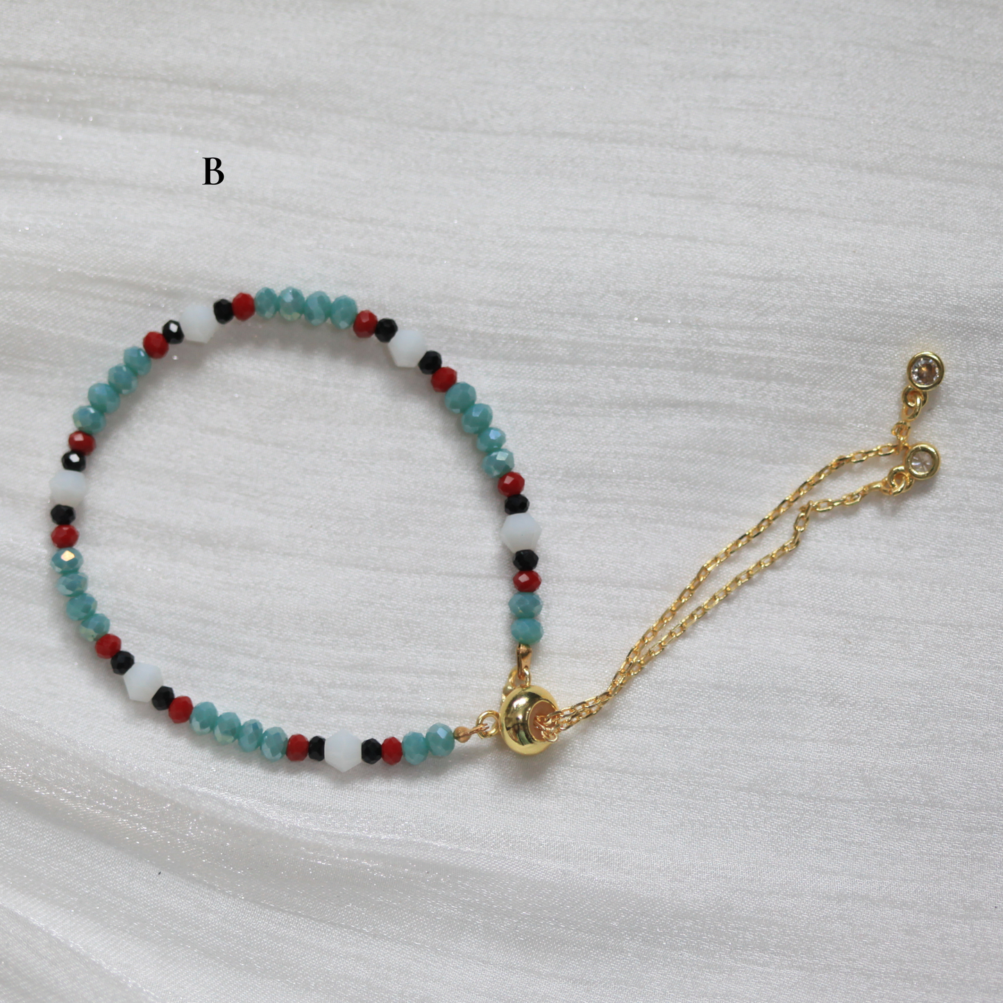 Multicolored beaded bracelet with a gold clasp on a light gray background. Tatreez Inspired.